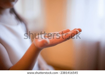 Close-up of a child's hand cradling intertwined wedding rings, bathed in soft light, evoking sentiments of innocence and cherished moments. Royalty-Free Stock Photo #2381416545