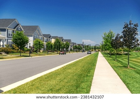 Quiet street in a residential area in the suburbs. Rows of houses along the sidewalk with a green lawn. Royalty-Free Stock Photo #2381432107