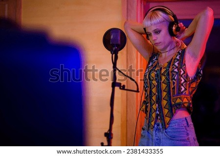 Professional female vocalist taking a break, stretching in front of a microphone in a recording studio. She is focusing before the next recording session. Portrait of a singer in a recording studio.
