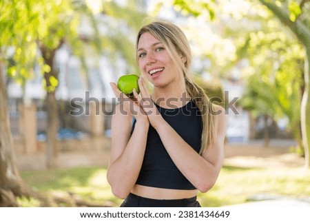 Young blonde woman at outdoors holding an apple