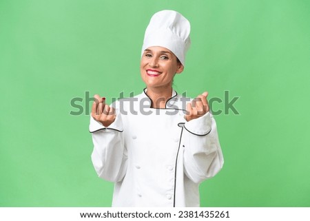Middle-aged chef woman over isolated background making money gesture