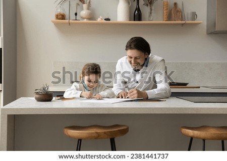 Happy cheerful father teaching to draw adorable little daughter girl. Dad and sweet kid enjoying home learning creative activity, making doodles in paper albums with colored pencils. Fatherhood