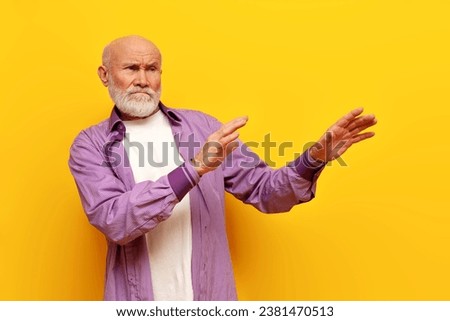 dissatisfied old bald grandfather with gray beard avoids and ignores on yellow isolated background, elderly pensioner rejects and refuses with hands Royalty-Free Stock Photo #2381470513
