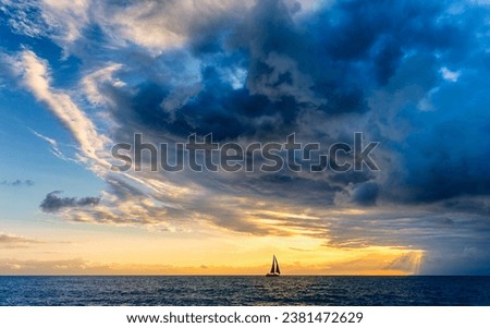 A Sailboat Is Approaching A Dark Looming Ocean Storm With Sun Rays Breaking Through Royalty-Free Stock Photo #2381472629