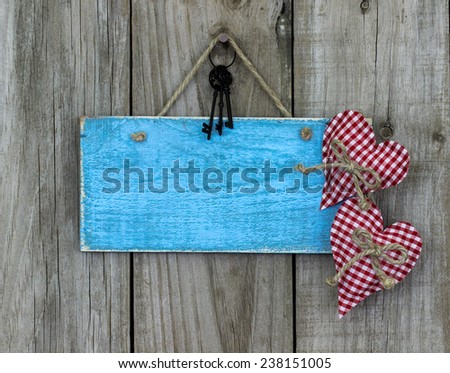 Blank antique teal blue sign with red gingham fabric hearts and black iron keys hanging on shabby wooden background