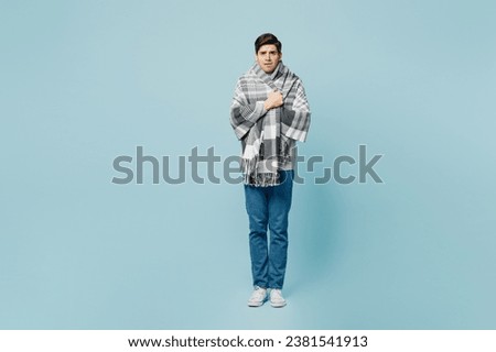 Full body sad shocked scared young ill sick man wrapped in gray plaid looking camera isolated on plain blue background studio. Healthy lifestyle disease virus treatment cold season recovery concept