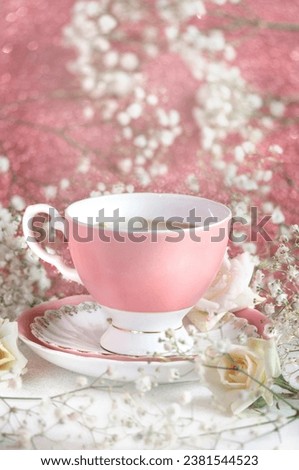 Coffee mug on a saucer in a composition with flowers on a pink background in vintage style. Daylight, selective focus with blurred background. Vertical image. greeting card