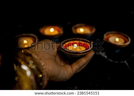 Happy Diwali - Woman hands with henna holding lit candle isolated on dark background. Clay Diya lamps lit during Dipavali, Hindu festival of lights celebration. Copy space for text.