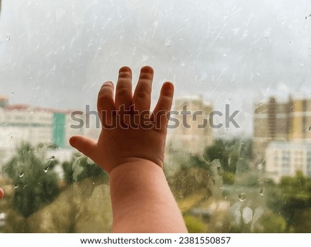 Baby's little hand on the cold glass of the window during the rain.