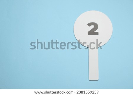 Auction paddle with number 2 on light blue background, top view. Space for text