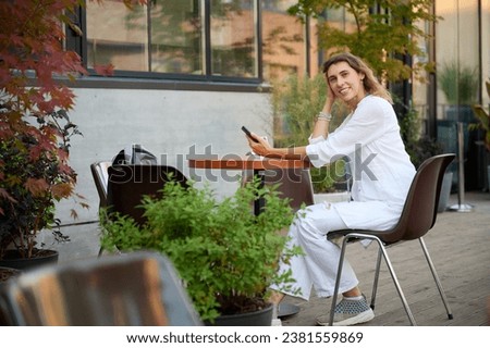 Portrait of a young attractive business woman sitting at a table in a cafe and texting on the phone, taking a selfie and browsing social networks