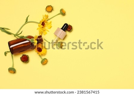 Bottle and pipette of essential oil near beautiful calendula flowers on yellow background, flat lay. Space for text