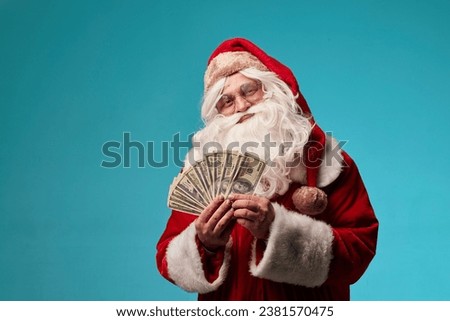 portrait of Santa Claus holding money dollars in his hands on a clean blue background, Santa gives out money