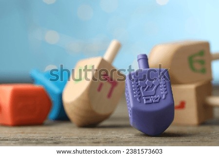 Hanukkah celebration. Dreidels with jewish letters on wooden table against light blue background with blurred lights, closeup