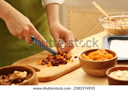 Making granola. Woman cutting dried apricots and cherries at table in kitchen, closeup Royalty-Free Stock Photo #2381574933