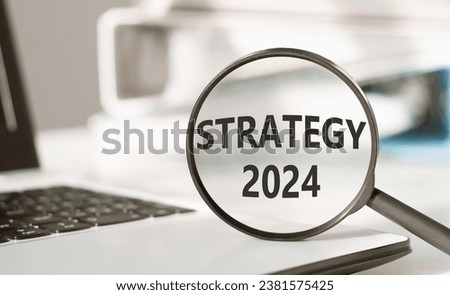 Magnifying glass with text STRATGY 2024 on office background. Focused on business concept. Search new idea for work