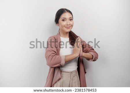 A smiling young Asian woman employee wearing a cardigan gestures a traditional greeting isolated over white background