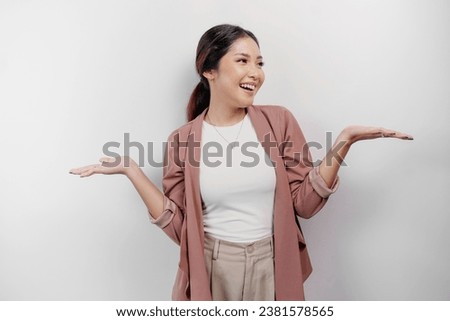 Excited Asian woman employee wearing cardigan pointing at the copy space beside her, isolated by white background Royalty-Free Stock Photo #2381578565