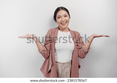 Excited Asian woman employee wearing cardigan pointing at the copy space beside her, isolated by white background Royalty-Free Stock Photo #2381578567