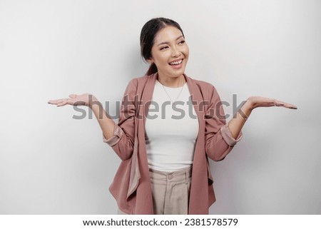 Excited Asian woman employee wearing cardigan pointing at the copy space beside her, isolated by white background Royalty-Free Stock Photo #2381578579