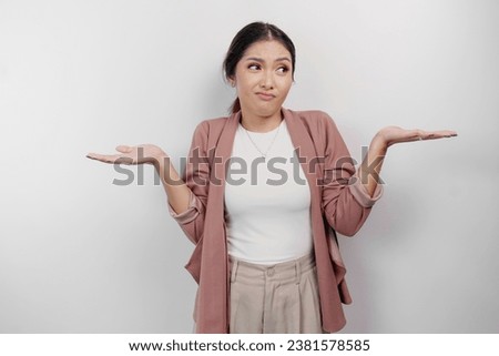 A thoughtful Asian woman employee wearing a cardigan is pointing to copy space beside her, looks so confused between choices, isolated by a white background 