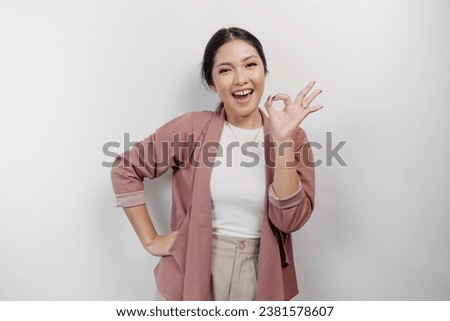 Excited Asian woman employee wearing a cardigan giving an OK hand gesture isolated by a white background