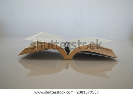 a book and a pen on a table with a white background Royalty-Free Stock Photo #2381579559