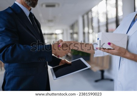Pharmaceutical sales representative shaking hand with female doctor in medical building. Hospital director consulting with healthcare staff. Royalty-Free Stock Photo #2381590023