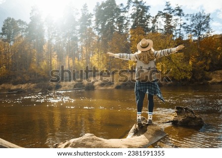 Beautiful woman traveler enjoying autumn hiking along the river. A traveler walks in the autumn forest, enjoying the weather. Active lifestyle. Royalty-Free Stock Photo #2381591355