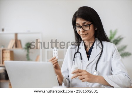 Hindu hospital worker talking to patient on video call and making consultation about treatment in bright office. Attentive nurse holding pills in hands and prescribing course of medication.