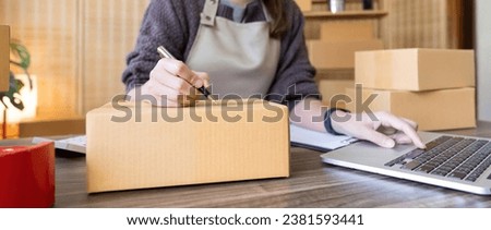 Woman is writing a list of customer on box before shipping to them, she runs an ecommerce business on websites and social media. Concept of selling products online