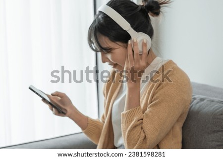 Happy Young Asian woman wearing headphone  listening to music relax in living room.