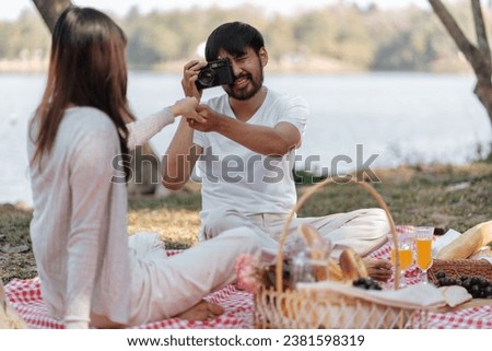 Happy asian couple travel. Man taking photo of his girlfriend picnic time in park holidays vacation 
