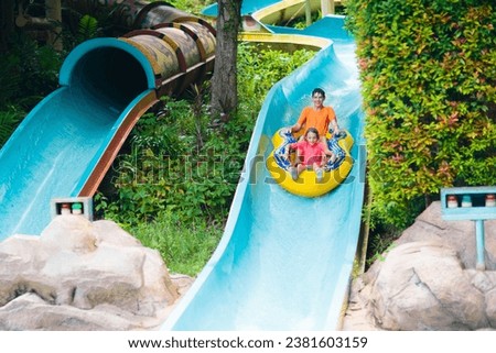 Kids on water slide in outdoor swimming pool. Family in aqua theme park. Children have fun in splash playground. Summer vacation with child. Kid on inflatable tube sliding into a pool. Royalty-Free Stock Photo #2381603159