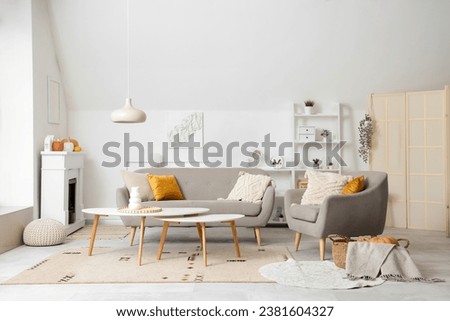 Interior of light living room with electric fireplace, armchair and sofa