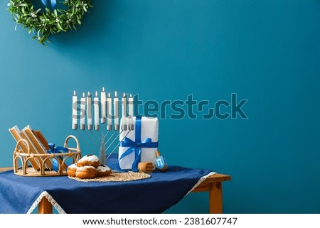 Menorah with donuts, books, dreidels and gift for Hannukah on table near blue wall