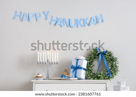 Menorah with doughnut, gift and wreath for Hannukah on commode in room