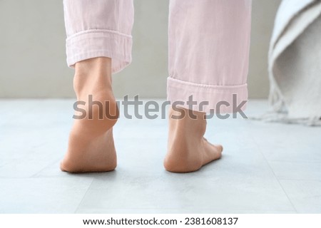 Barefoot woman walking on floor with heating in bedroom, back view