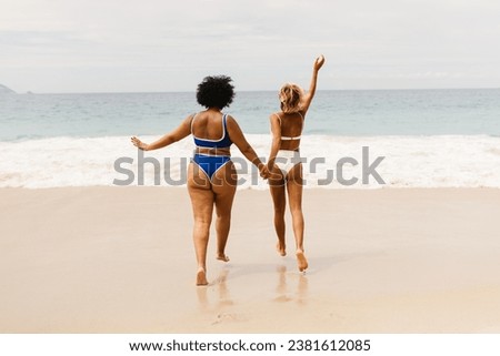 Women in bikinis running towards the waves at the beach, celebrating the spirit of a summer vacation. Two young girlfriends having fun together on an exciting beach holiday.