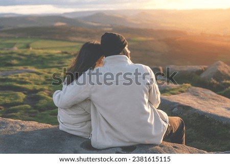 Back view of the happy couple in love sitting on top of a mountain enjoying a sunset landscape view toned image