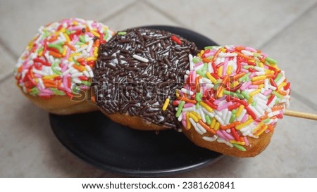 donuts with colorful sprinkles and chocolate sprinkles on skewers like satay on a black plate