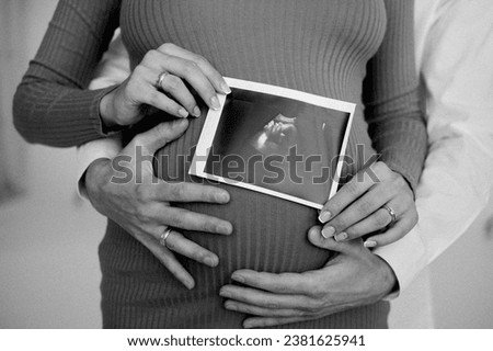 A pregnant woman holds an ultrasound picture of her baby in her hands. a man hugs a pregnant woman. young parents