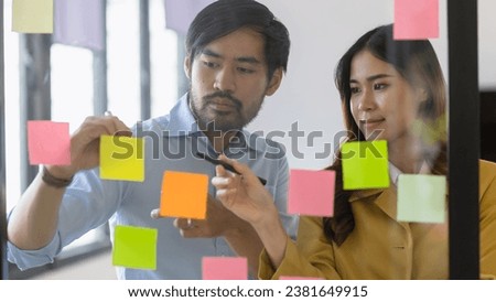 Two Asian businessman and woman working with sticky note on glass wall, Business startup project process concept. 