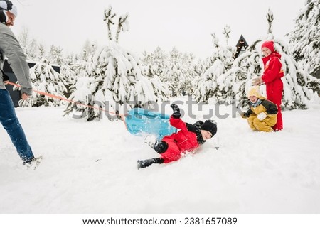 Kid fall into snow, lie. Dad pulling little son on winter day. Children are rolling down hill on sledge in forest. Happy child with father ride sled on snowy road. Family walks during snowfall in park