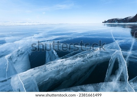 Baikal Lake in winter. An unusual landscape of the frozen Small Sea with clean transparent blue thick ice with beautiful cracks in the depths. Amazing winter travel. Natural cold background Royalty-Free Stock Photo #2381661499