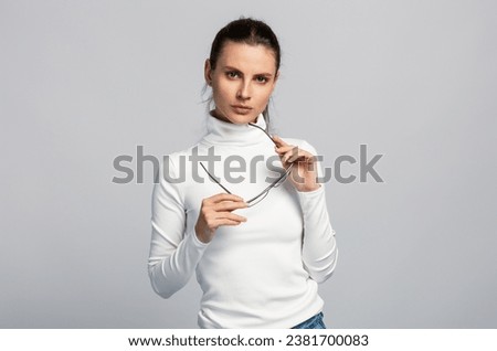 Portrait of an attractive woman with glasses, white top, business style, on light grey studio background