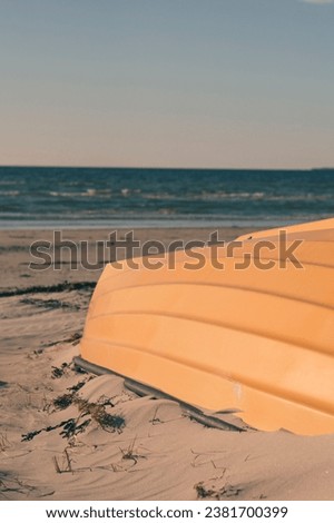 An orange sailing boat is pictured on a sandy beach in a coastal area, with the ocean visible in the background