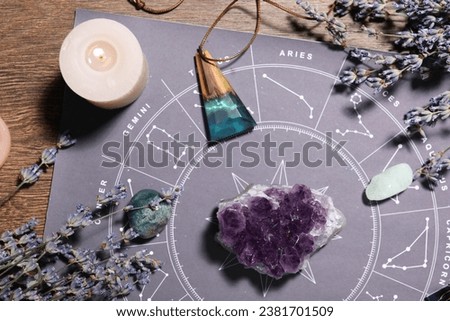Astrology prediction. Zodiac wheel, gemstones, burning candle and lavender on wooden table, flat lay