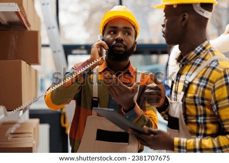 Warehouse logistics operator managing parcel dispatching on telephone. African american shipment managers asking about goods delivery in factory industrial storehouse on landline phone Royalty-Free Stock Photo #2381707675