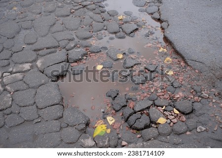 Damaged asphalt road surface on an autumn rainy day close-up, road repair is needed